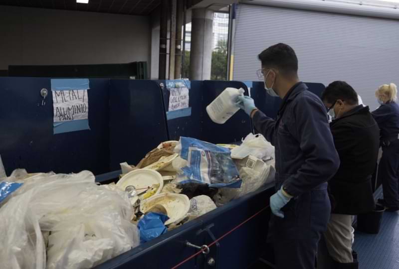 Convention Center employee tosses bottle into a bin on a crowded sorter conveyor belt