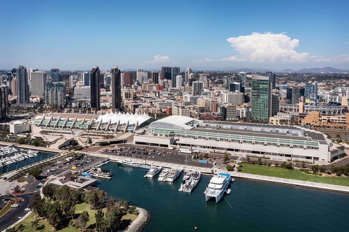 Aerial image of the San Diego Convention Center building, San Diego skyline, and boats along the bay.