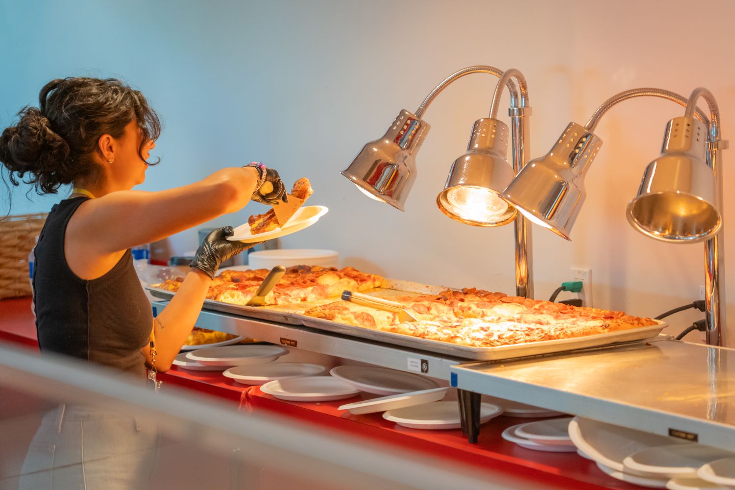 Woman placing a slice of hot pizza on a plate at a concession stand